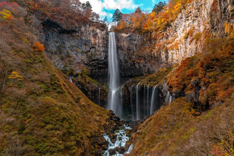 Tall Nikko waterfall cascading down rocky cliffs surrounded by autumn colors.